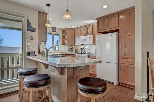 kitchen with a kitchen bar, a sink, white appliances, a peninsula, and light countertops