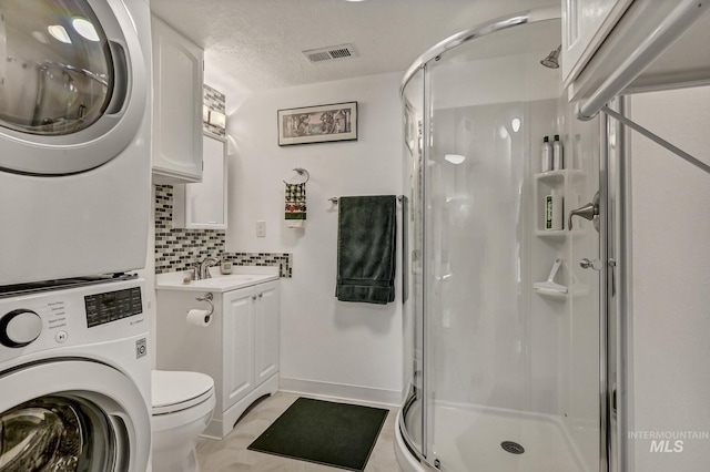 bathroom with tasteful backsplash, visible vents, a shower stall, stacked washing maching and dryer, and a textured ceiling