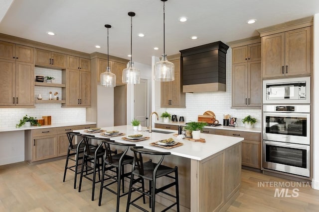 kitchen featuring sink, a breakfast bar area, hanging light fixtures, a center island with sink, and stainless steel double oven