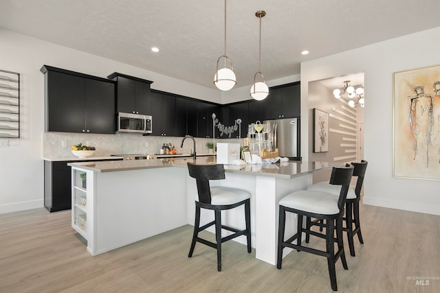 kitchen featuring backsplash, stainless steel appliances, decorative light fixtures, light hardwood / wood-style flooring, and a large island