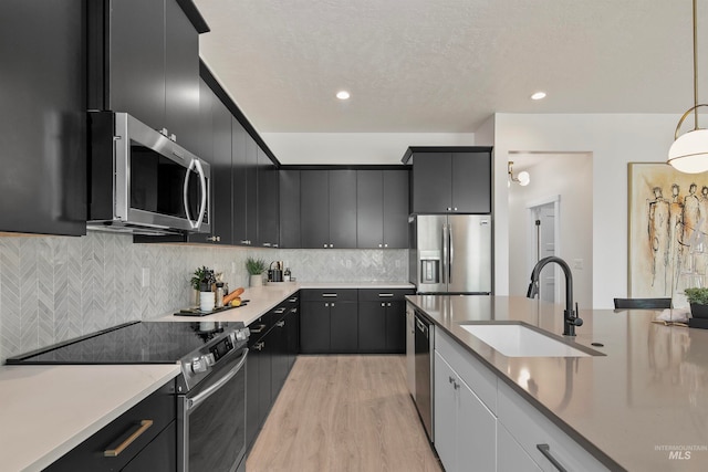 kitchen with appliances with stainless steel finishes, tasteful backsplash, sink, light hardwood / wood-style floors, and hanging light fixtures