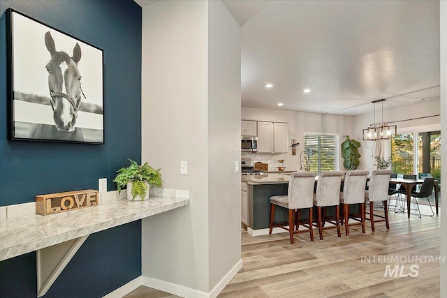 kitchen featuring pendant lighting, white cabinets, range, backsplash, and a breakfast bar