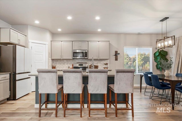 kitchen with a center island with sink, appliances with stainless steel finishes, tasteful backsplash, a kitchen breakfast bar, and pendant lighting