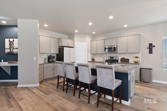 kitchen with stainless steel appliances, an island with sink, decorative backsplash, light wood-type flooring, and a breakfast bar