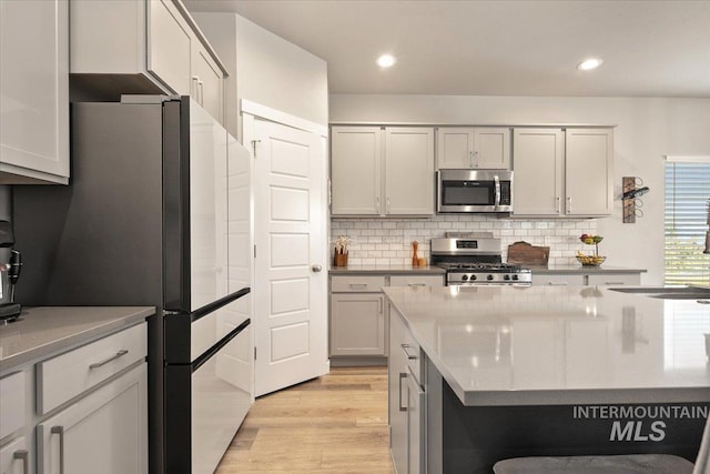 kitchen with stainless steel appliances, gray cabinetry, tasteful backsplash, light hardwood / wood-style flooring, and sink