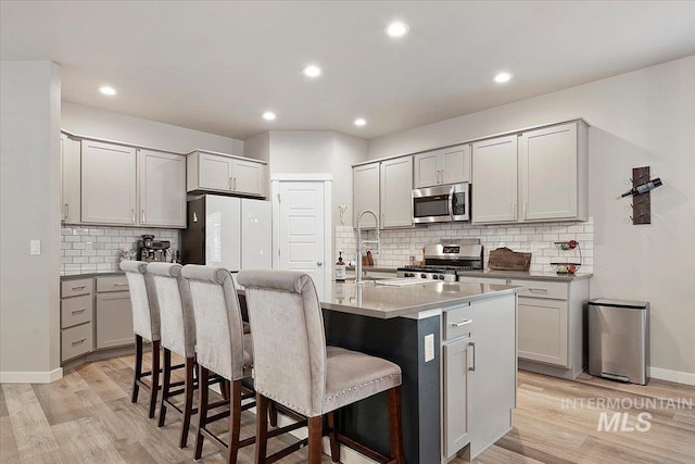 kitchen featuring appliances with stainless steel finishes, tasteful backsplash, a kitchen island with sink, light wood-type flooring, and a breakfast bar area