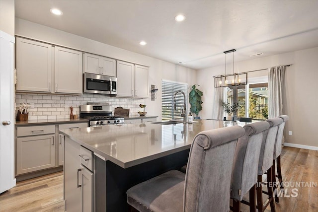 kitchen with pendant lighting, a center island with sink, sink, light hardwood / wood-style flooring, and appliances with stainless steel finishes