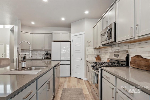 kitchen with light wood-type flooring, appliances with stainless steel finishes, tasteful backsplash, and sink