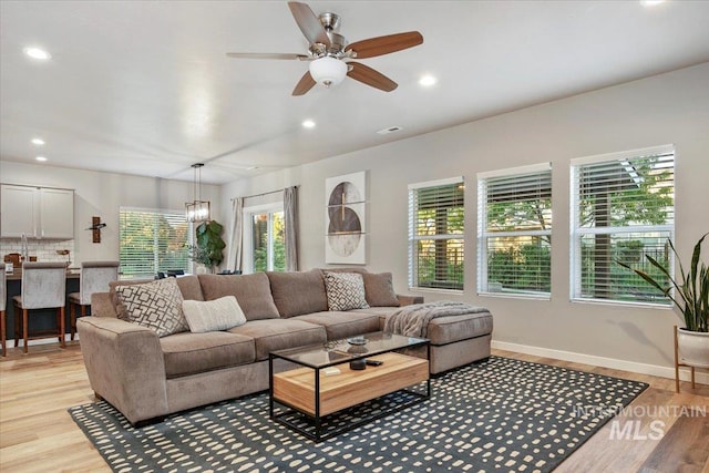 living room with ceiling fan with notable chandelier and light hardwood / wood-style flooring