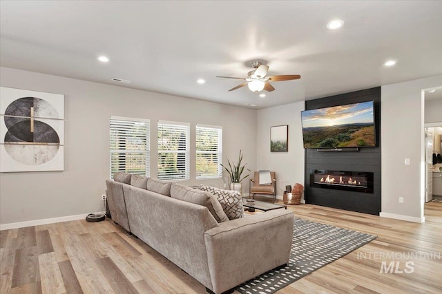 living room featuring ceiling fan, a large fireplace, and light hardwood / wood-style floors