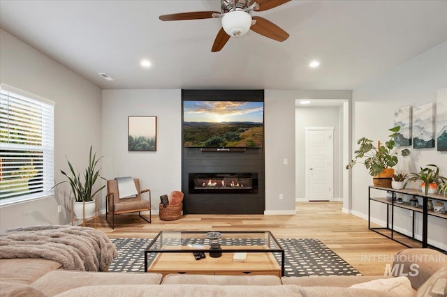 living room featuring ceiling fan, a fireplace, and light hardwood / wood-style flooring