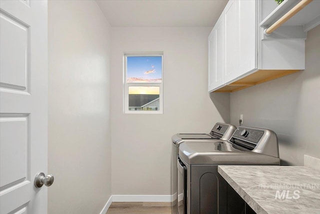 washroom featuring light wood-type flooring, washing machine and clothes dryer, and cabinets