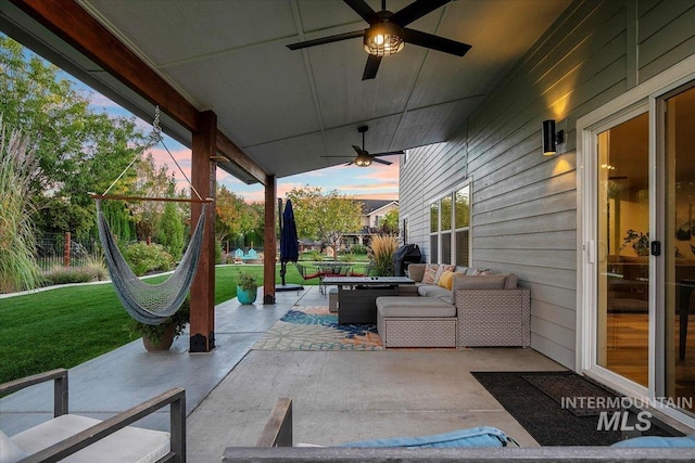 patio terrace at dusk with an outdoor living space, a yard, and ceiling fan