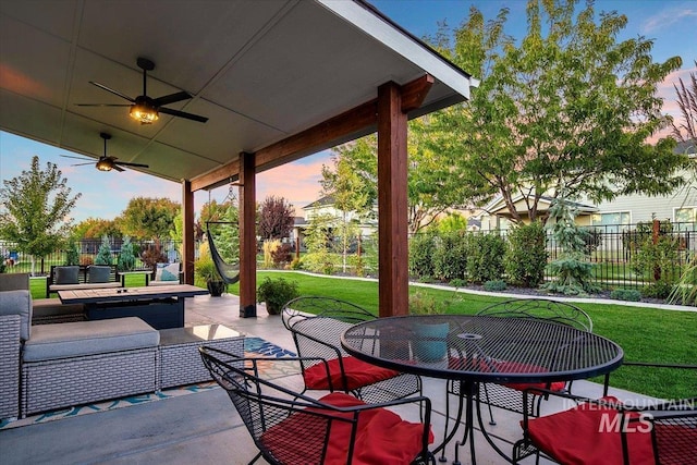 patio terrace at dusk featuring ceiling fan, an outdoor living space, and a yard