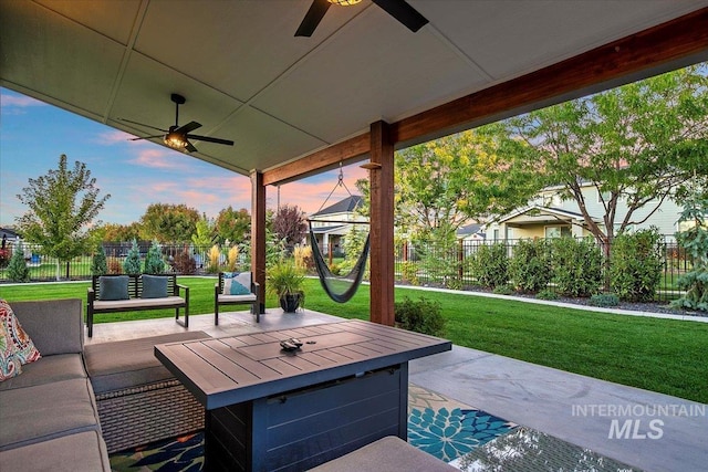 patio terrace at dusk featuring ceiling fan, an outdoor living space, and a yard