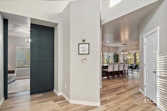 corridor featuring an inviting chandelier, a wealth of natural light, and light hardwood / wood-style floors