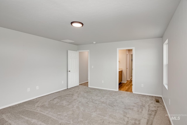 unfurnished bedroom featuring ensuite bathroom and light colored carpet