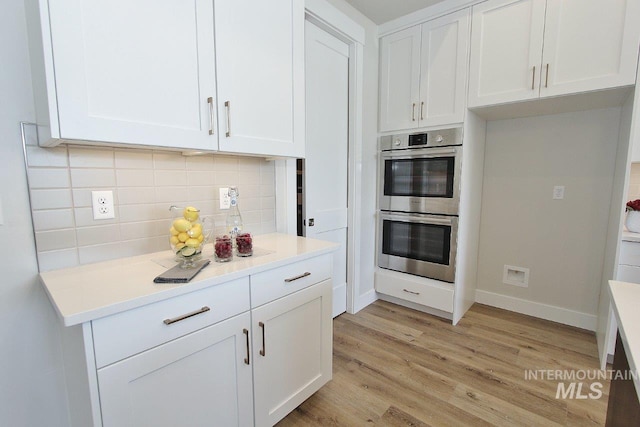 kitchen with light hardwood / wood-style floors, backsplash, white cabinetry, and double oven