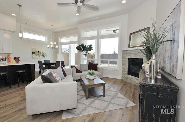 living room with ceiling fan with notable chandelier, hardwood / wood-style floors, and a tile fireplace