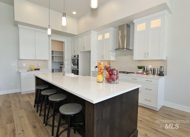 kitchen with white cabinets, a kitchen island with sink, and wall chimney range hood