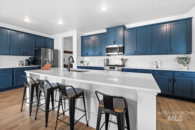 kitchen with light wood finished floors, a sink, appliances with stainless steel finishes, a kitchen breakfast bar, and blue cabinets