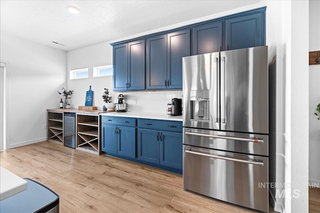 kitchen with blue cabinets, light wood-style flooring, stainless steel refrigerator with ice dispenser, backsplash, and light countertops