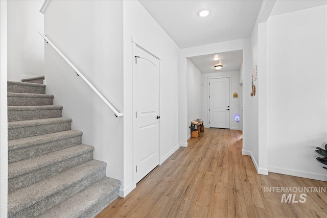 hallway with light wood-style flooring, stairs, and baseboards