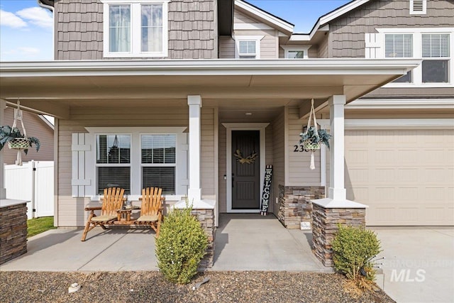 doorway to property with stone siding, covered porch, concrete driveway, and fence