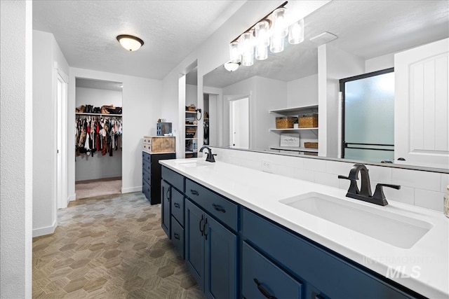 full bathroom with a sink, a walk in closet, a textured ceiling, and decorative backsplash