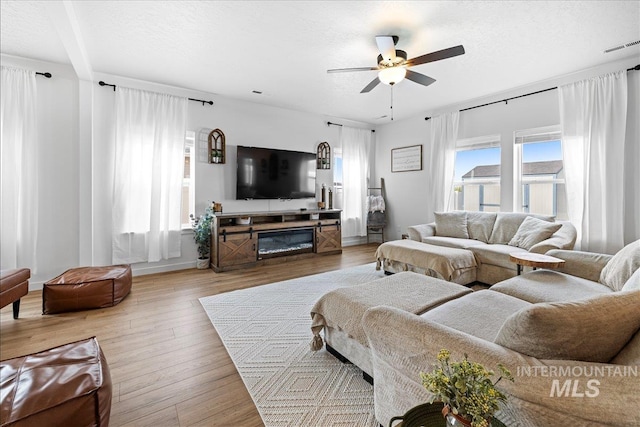 living room with a textured ceiling, visible vents, light wood finished floors, and ceiling fan