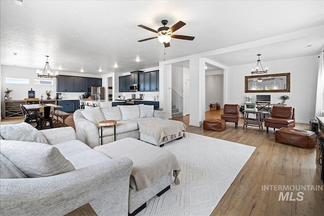 living room with baseboards, stairs, hardwood / wood-style flooring, a textured ceiling, and ceiling fan with notable chandelier