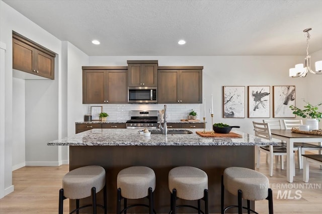 2252 E Tiger Lily Dr, Boise, ID 83716 - kitchen with stainless steel appliances, decorative backsplash, a sink, light wood-style flooring, and a kitchen bar