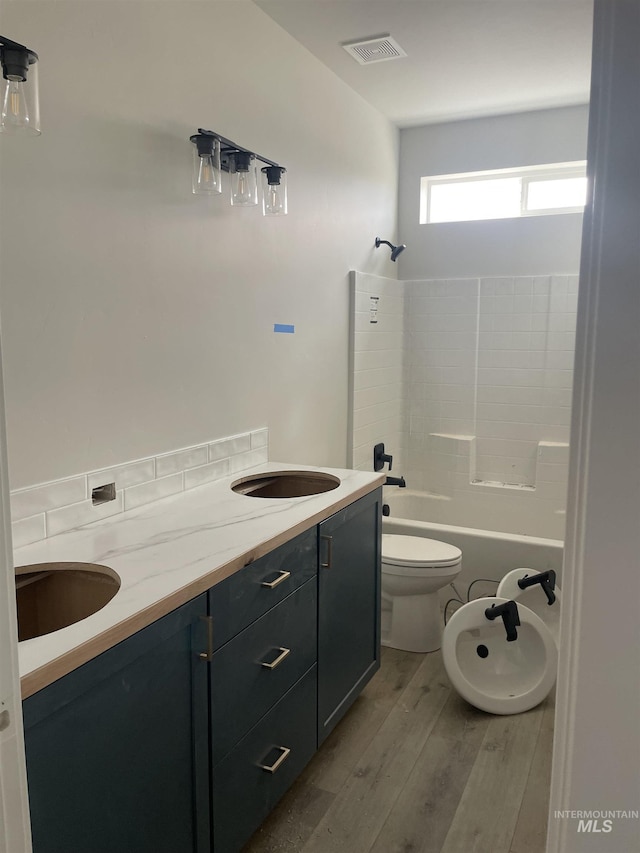 bathroom featuring visible vents, toilet, shower / bath combination, wood finished floors, and vanity