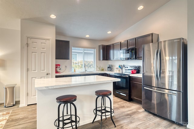 kitchen featuring black appliances, a breakfast bar, a center island, dark brown cabinetry, and lofted ceiling