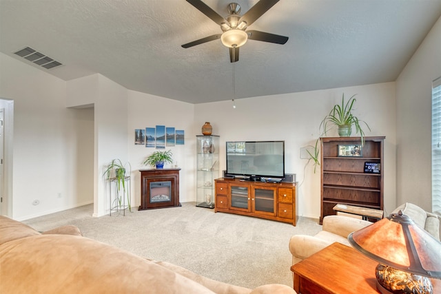 carpeted living area with a ceiling fan, a textured ceiling, baseboards, and a glass covered fireplace