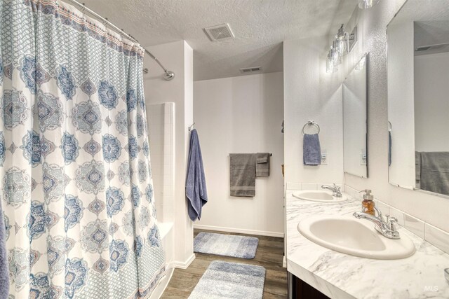 bathroom with wood finished floors, a textured ceiling, baseboards, and double vanity