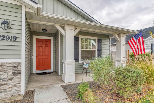 doorway to property with stone siding, board and batten siding, and covered porch