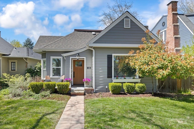 bungalow with fence, roof with shingles, and a front lawn