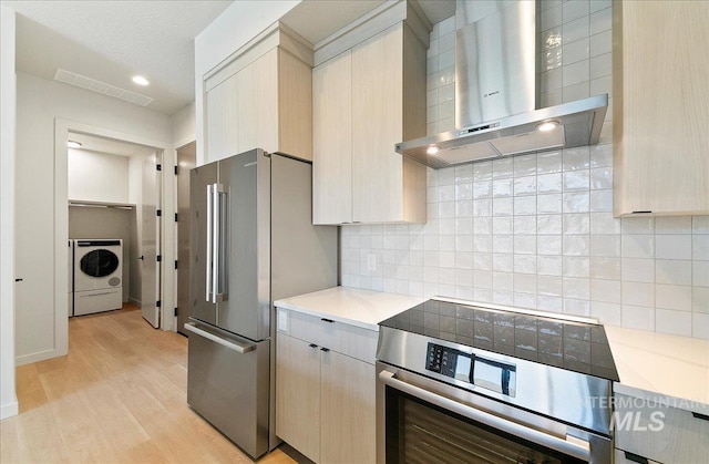 4340 E Haystack St Unit 304, Boise, ID 83716 - kitchen with wall chimney range hood, washer / clothes dryer, appliances with stainless steel finishes, light wood-style floors, and decorative backsplash