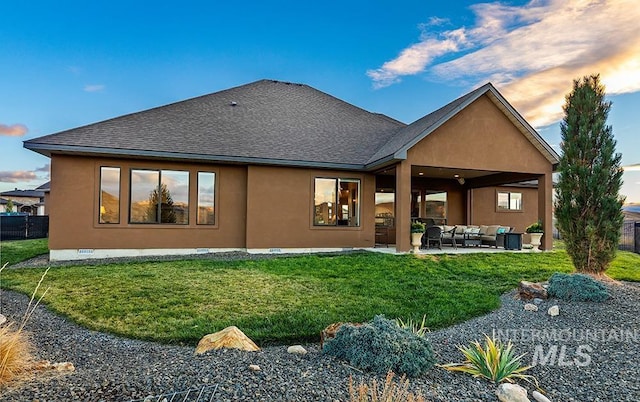 back house at dusk featuring an outdoor living space, a lawn, and a patio