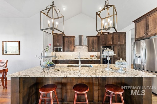 kitchen featuring appliances with stainless steel finishes, a kitchen breakfast bar, hanging light fixtures, and wall chimney range hood