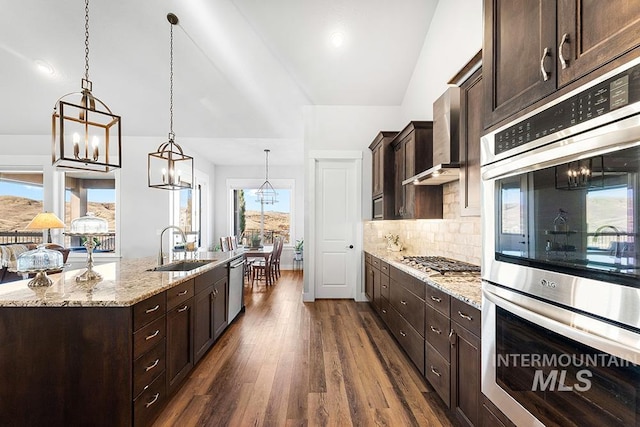 kitchen featuring pendant lighting, sink, light stone counters, stainless steel appliances, and a center island with sink