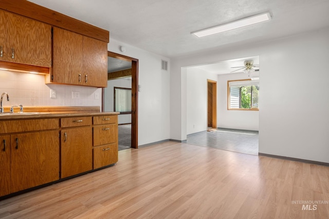 kitchen featuring backsplash, light wood finished floors, brown cabinetry, and a sink