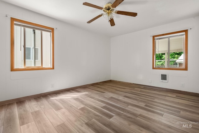 empty room featuring a ceiling fan, light wood-style floors, heating unit, and baseboards