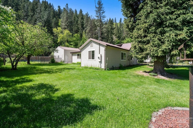 exterior space featuring metal roof, fence, a forest view, and a yard