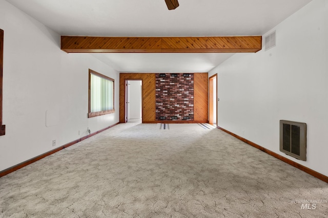 carpeted spare room with baseboards, ceiling fan, wooden walls, and visible vents