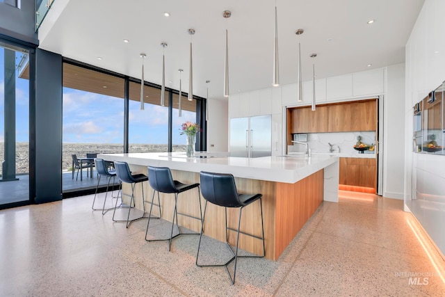 kitchen featuring tasteful backsplash, a spacious island, hanging light fixtures, built in fridge, and white cabinetry