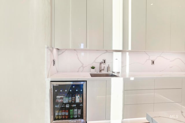 bar featuring beverage cooler, tasteful backsplash, light stone counters, sink, and white cabinets