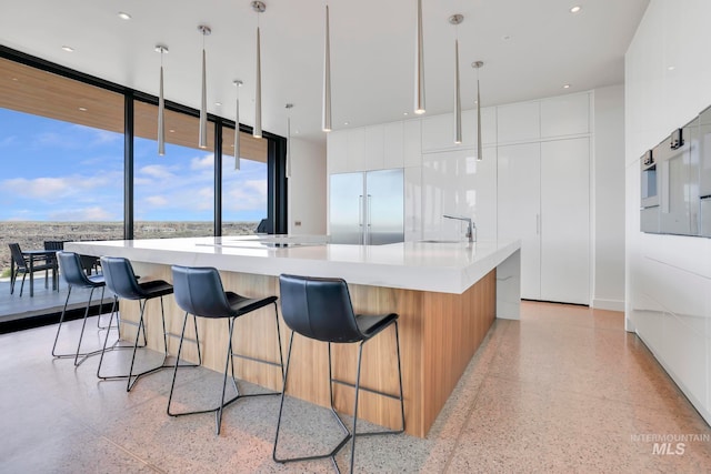 kitchen featuring stainless steel built in refrigerator, pendant lighting, a large island, sink, and white cabinets