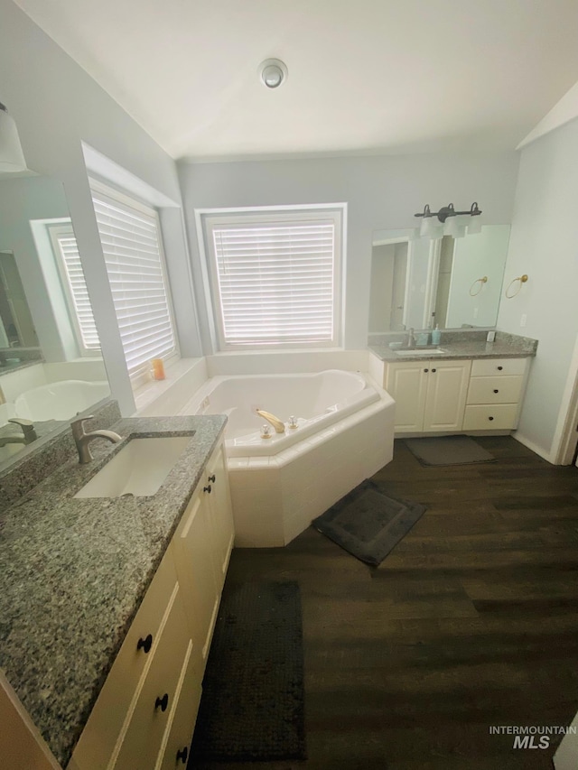 bathroom featuring a sink, two vanities, a garden tub, and wood finished floors